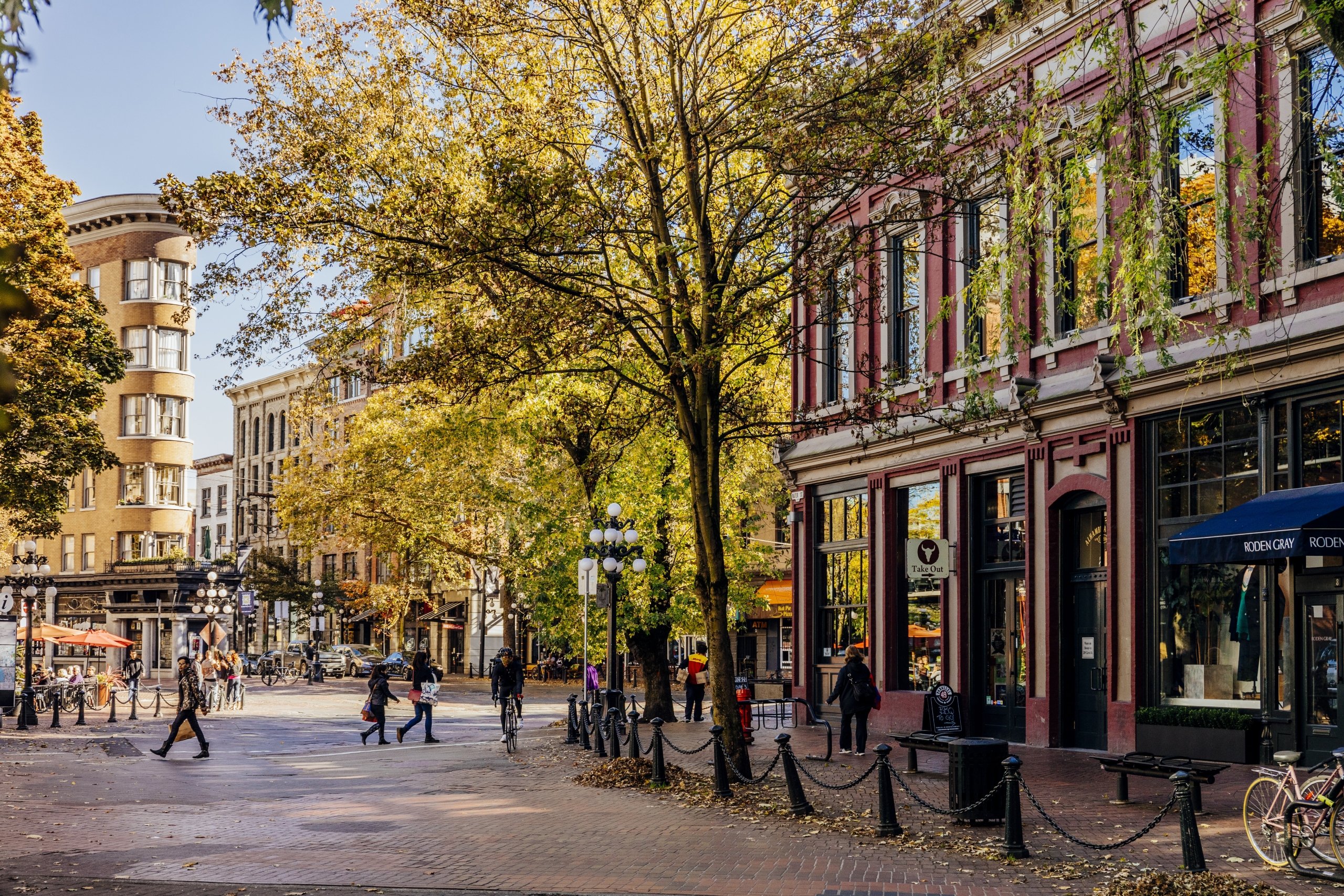 Street view of gastown, with the brick streets and people walking around, it is a wide shot with a few buildings and trees in all across the middle image, with the street taking up much of the foreground.
