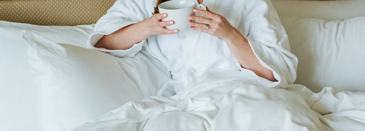 A woman drinking coffee with a breakfast tray in bed.