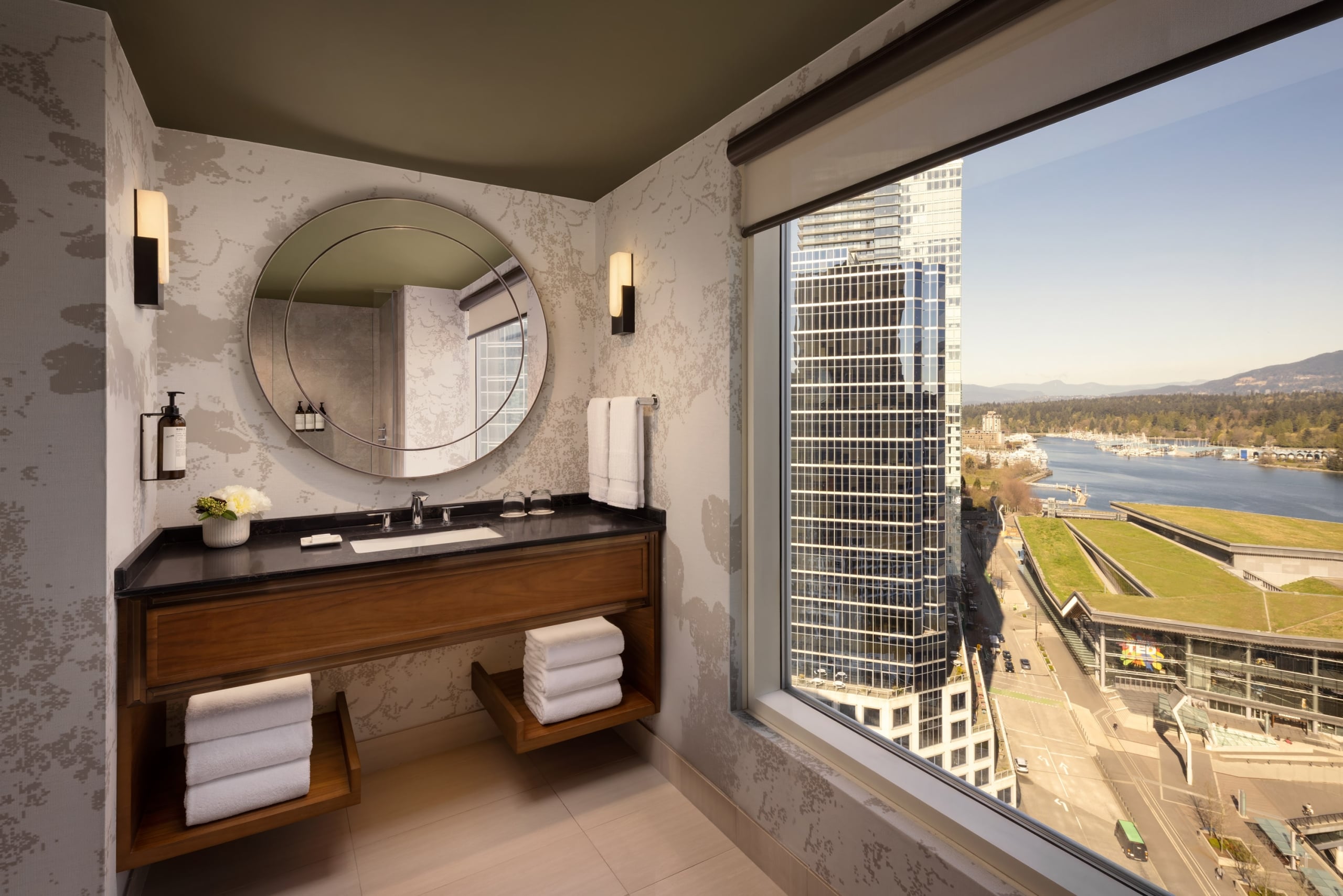 Newly renovated bathroom at Fairmont Waterfront featuring a walk-in glass shower, modern coastal design, and a large window with harbour views, creating a bright, light-filled space in downtown Vancouver.