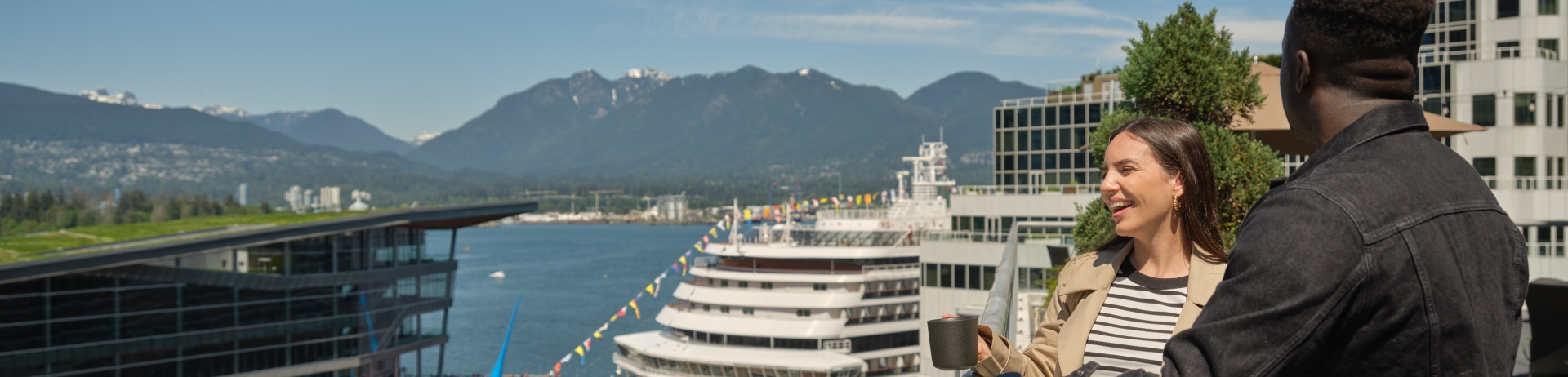 Couple looking out over Vancouver's harbour from Fairmont Waterfront's Fairmont Gold terrace with cruise ship in background.
