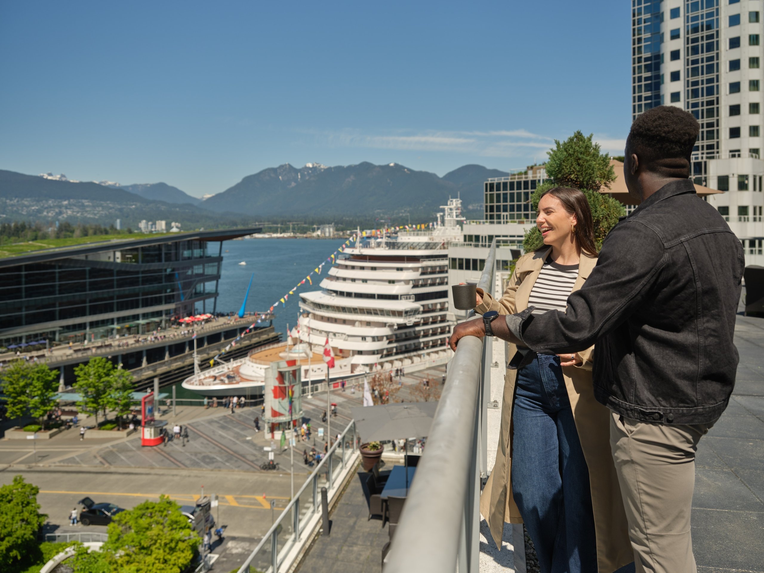 Couple looking out over Vancouver's harbour from Fairmont Waterfront's Fairmont Gold terrace with cruise ship in background.