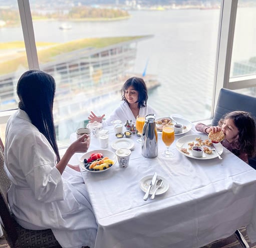 A mother and two daughters eating breakfast with a view of a cruise ship.