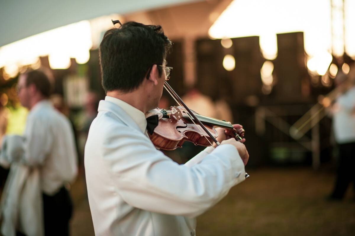 Man in white dress shirt standing and playing a violin, shot from behind him.