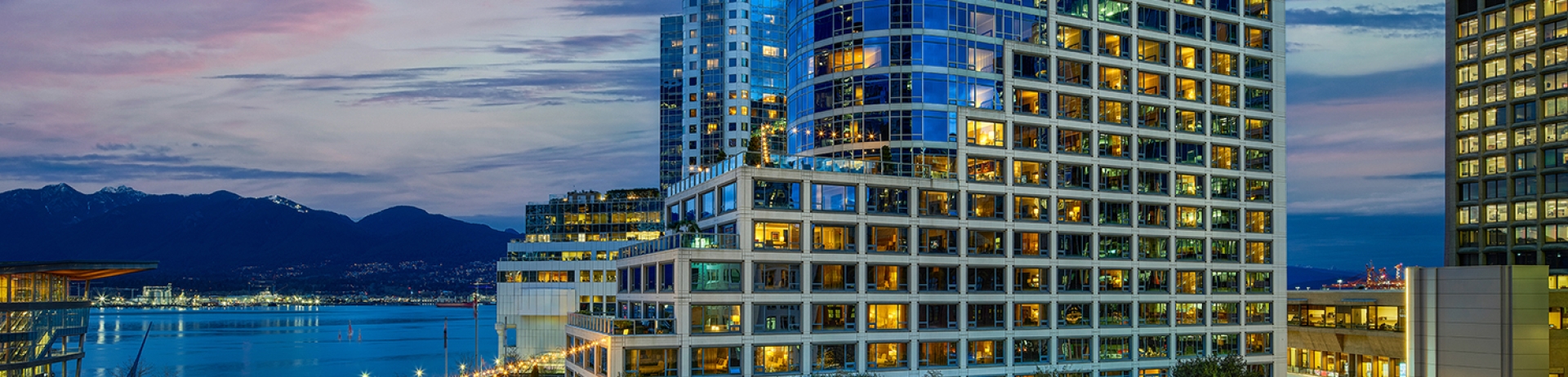Exterior of Fairmont Waterfront hotel set against the harbour and coastal mountains.