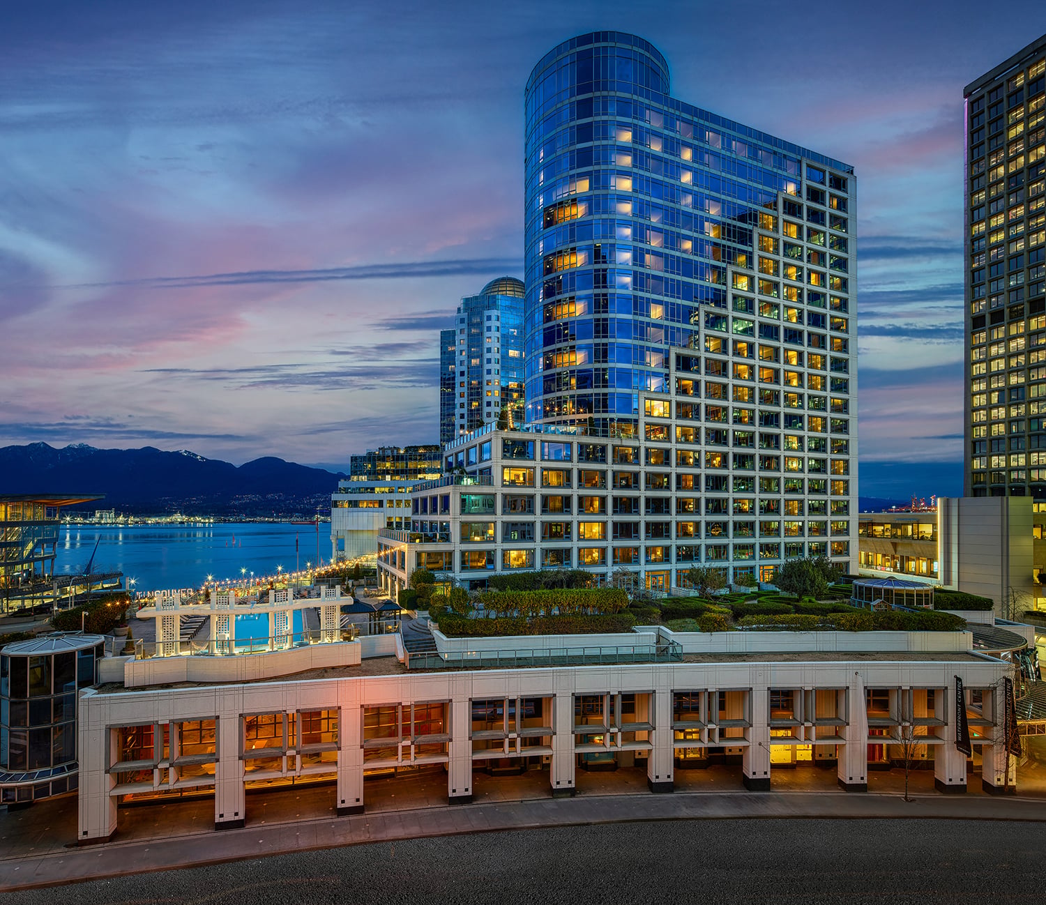 Exterior of Fairmont Waterfront hotel set against the harbour and coastal mountains.