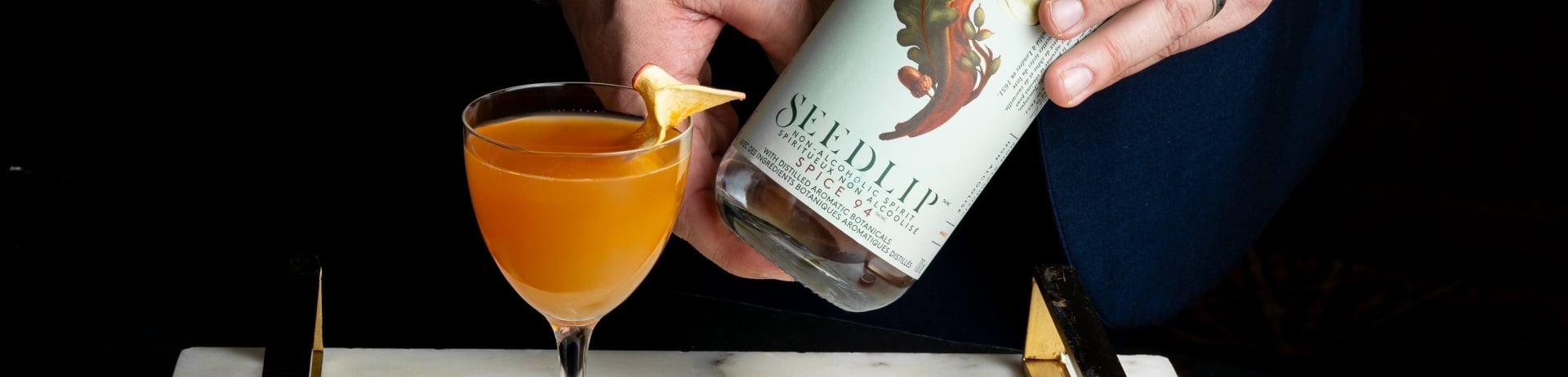 Bartender holding a bottle of Seedlip behind a spirit-free cocktail on a tray.